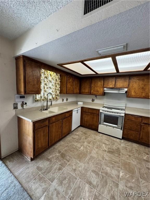 kitchen with white appliances, light countertops, a textured ceiling, under cabinet range hood, and a sink