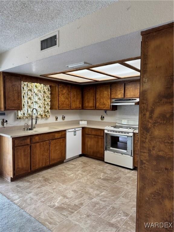 kitchen featuring white appliances, visible vents, light countertops, under cabinet range hood, and a sink