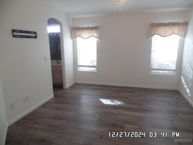 unfurnished dining area with arched walkways, dark wood-type flooring, a ceiling fan, and baseboards