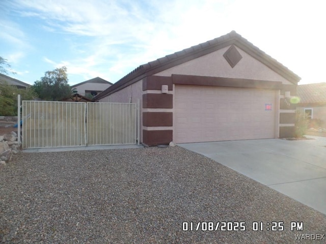 view of front of house featuring a tile roof, stucco siding, concrete driveway, a gate, and a garage