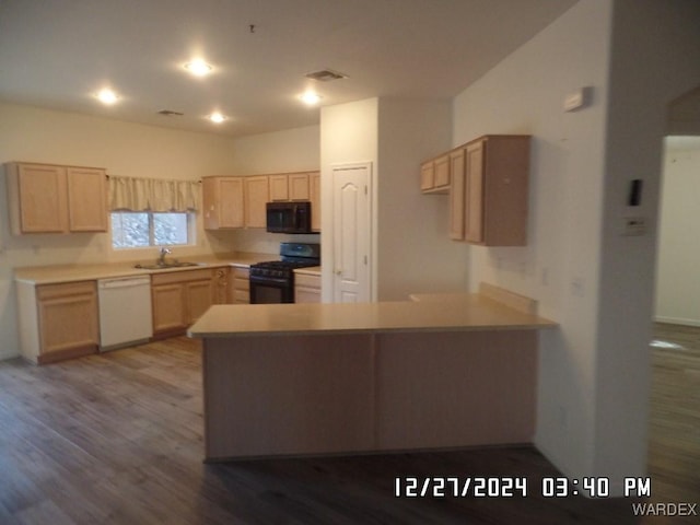 kitchen featuring a peninsula, light countertops, light brown cabinetry, black appliances, and a sink