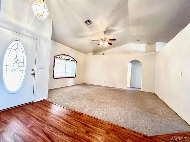 carpeted entryway with arched walkways, lofted ceiling, wood finished floors, visible vents, and a ceiling fan