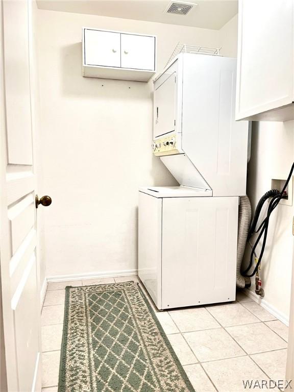 laundry room with light tile patterned floors, stacked washer / dryer, cabinet space, and visible vents