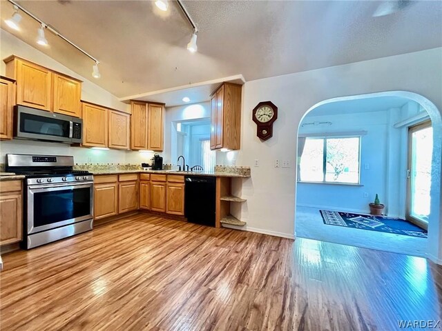 kitchen featuring light wood-type flooring, light stone countertops, appliances with stainless steel finishes, and a sink