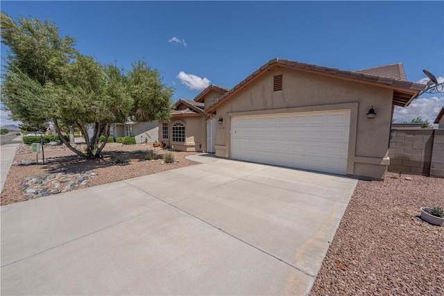 view of front of home with stucco siding, driveway, a garage, a tile roof, and fence