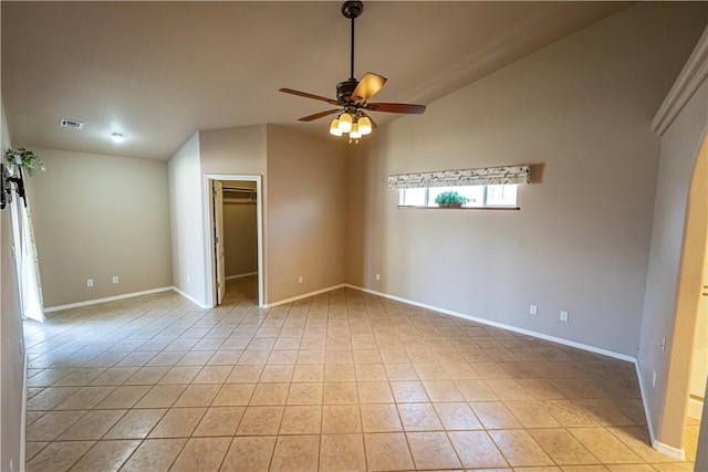 unfurnished bedroom featuring vaulted ceiling, baseboards, a walk in closet, light tile patterned floors, and ceiling fan