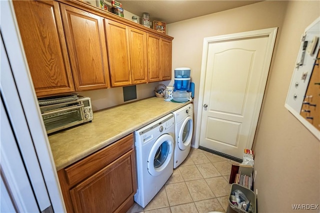 clothes washing area featuring cabinet space, light tile patterned floors, and washer and clothes dryer