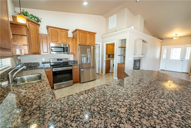 kitchen featuring stainless steel appliances, a sink, washer / clothes dryer, open shelves, and brown cabinetry