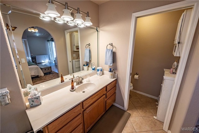 ensuite bathroom featuring connected bathroom, toilet, vanity, baseboards, and tile patterned floors