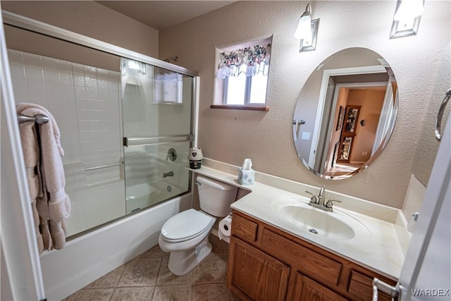 bathroom with bath / shower combo with glass door, a textured wall, toilet, vanity, and tile patterned floors