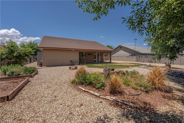 back of property with fence, a tile roof, a vegetable garden, and stucco siding