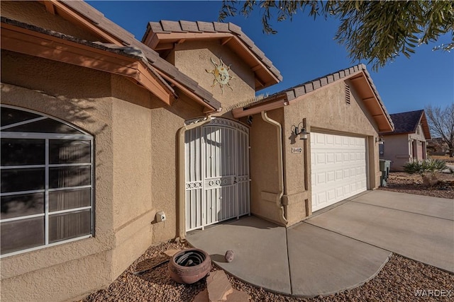 view of home's exterior with a gate, concrete driveway, an attached garage, and stucco siding