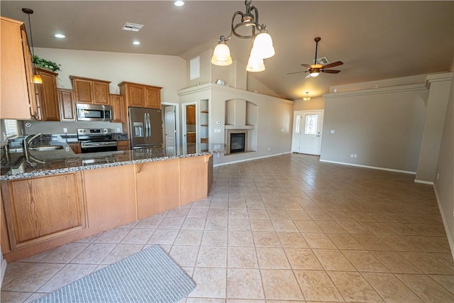 kitchen with stainless steel appliances, a sink, a ceiling fan, dark stone countertops, and light tile patterned flooring