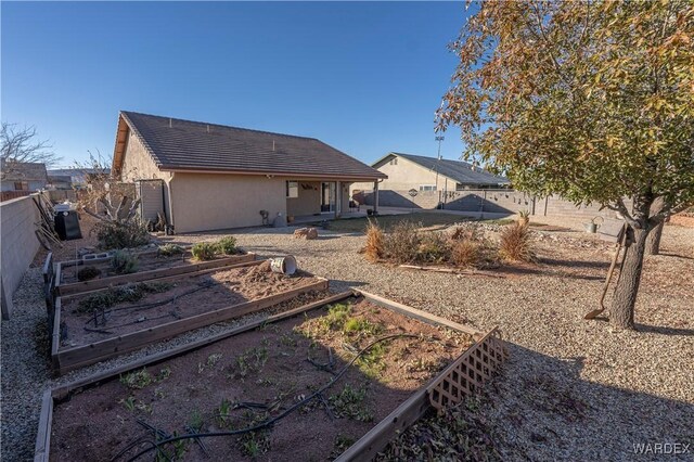 rear view of property featuring a fenced backyard, a vegetable garden, and stucco siding