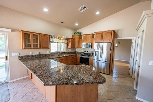 kitchen featuring appliances with stainless steel finishes, lofted ceiling, brown cabinets, a peninsula, and a sink