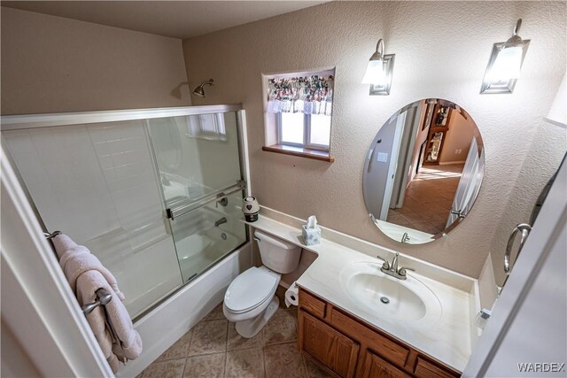 full bathroom featuring bath / shower combo with glass door, a textured wall, toilet, vanity, and tile patterned flooring