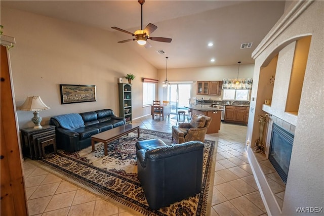 living area featuring light tile patterned floors, visible vents, a ceiling fan, vaulted ceiling, and a tile fireplace