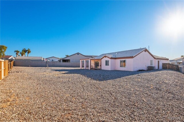 rear view of house with central AC, a fenced backyard, a tiled roof, and stucco siding