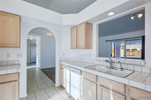 kitchen featuring arched walkways, dishwasher, tile countertops, light brown cabinetry, and a sink