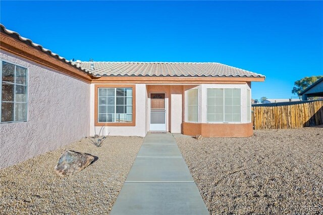 view of exterior entry featuring a tiled roof, fence, and stucco siding