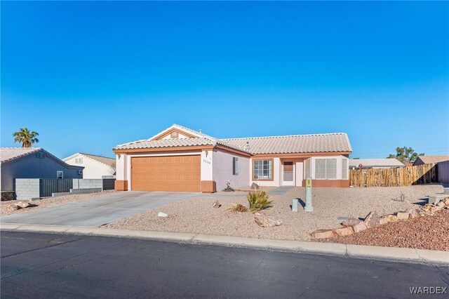 view of front of home with concrete driveway, a tiled roof, an attached garage, fence, and stucco siding