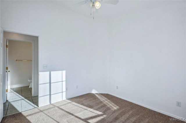 carpeted spare room with ceiling fan, baseboards, and tile patterned floors