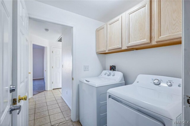 clothes washing area featuring cabinet space, light tile patterned flooring, and washing machine and clothes dryer