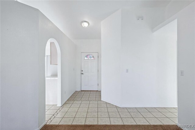 foyer entrance with arched walkways, baseboards, and light tile patterned floors