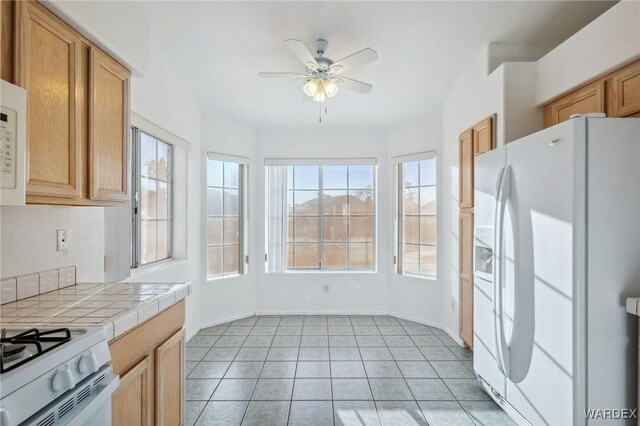 kitchen featuring tile countertops, light tile patterned floors, a ceiling fan, white appliances, and baseboards