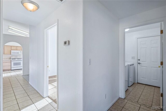 hallway with washing machine and dryer, arched walkways, and light tile patterned floors