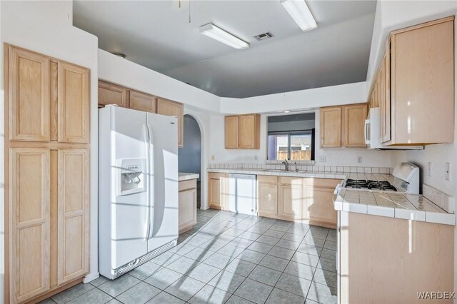 kitchen featuring white appliances, visible vents, a sink, and light brown cabinetry