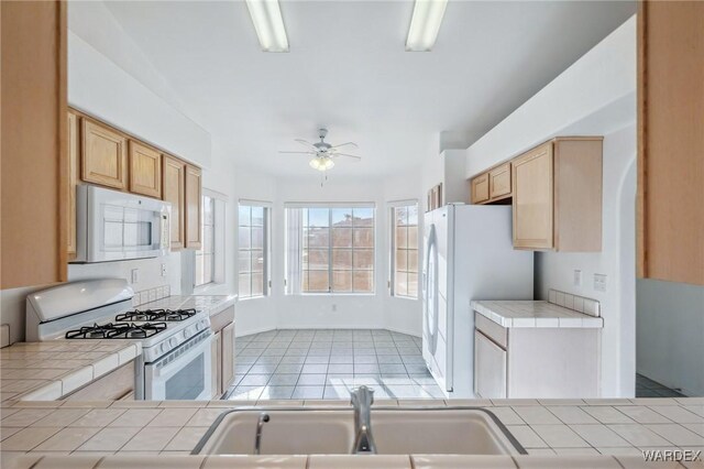 kitchen with white appliances, tile counters, and a sink