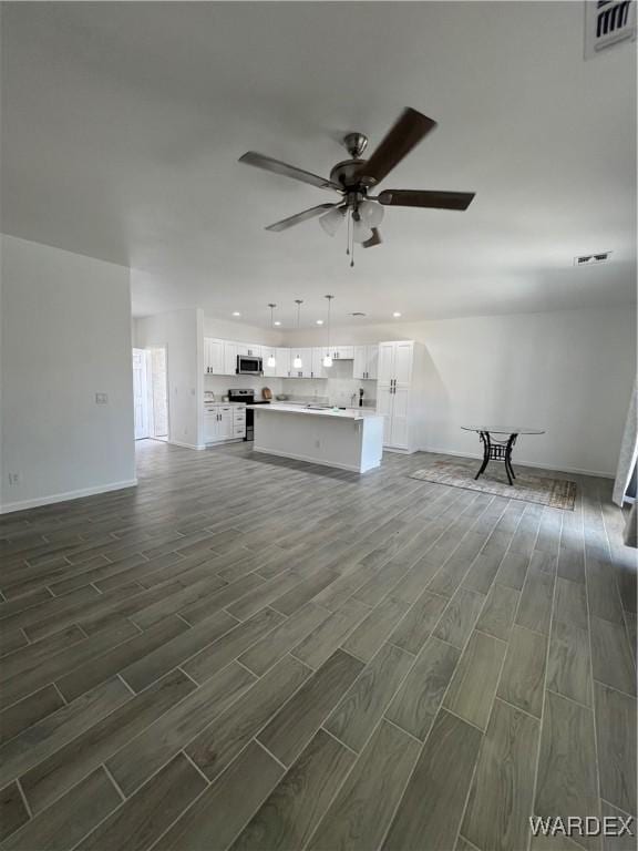 unfurnished living room featuring baseboards, wood finish floors, visible vents, and a ceiling fan