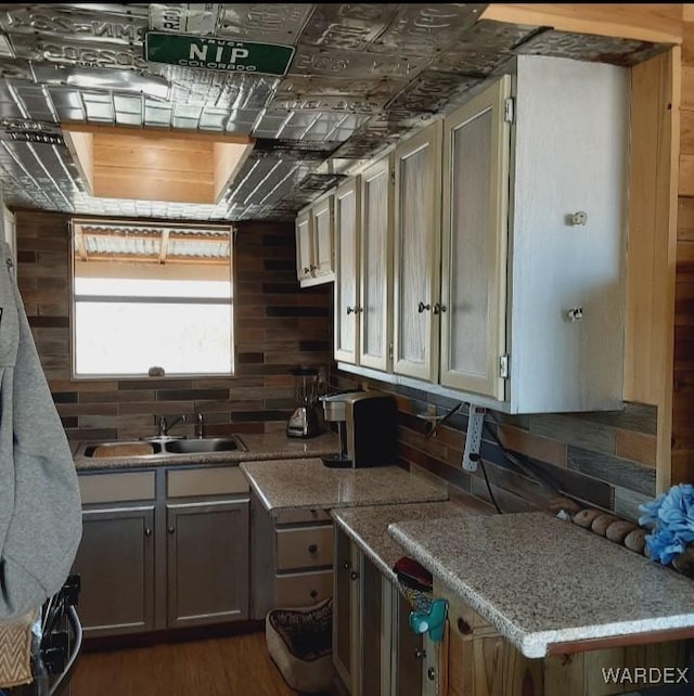 kitchen featuring light stone countertops, dark wood-style floors, decorative backsplash, and a sink