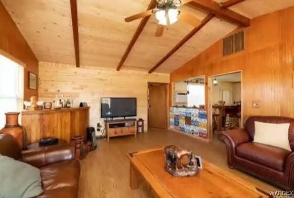 living area featuring vaulted ceiling with beams, ceiling fan, wooden walls, and visible vents