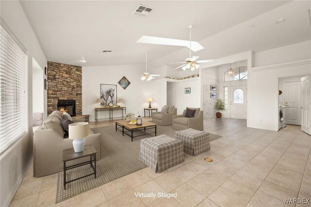 living area featuring a fireplace, light tile patterned floors, visible vents, lofted ceiling with skylight, and washer / dryer