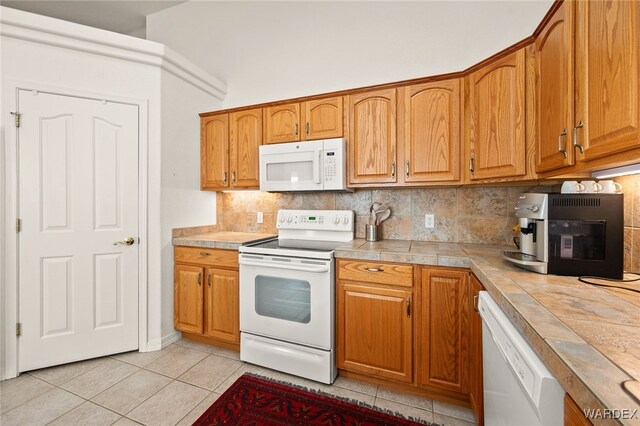 kitchen featuring white appliances, tile counters, brown cabinets, and light tile patterned flooring