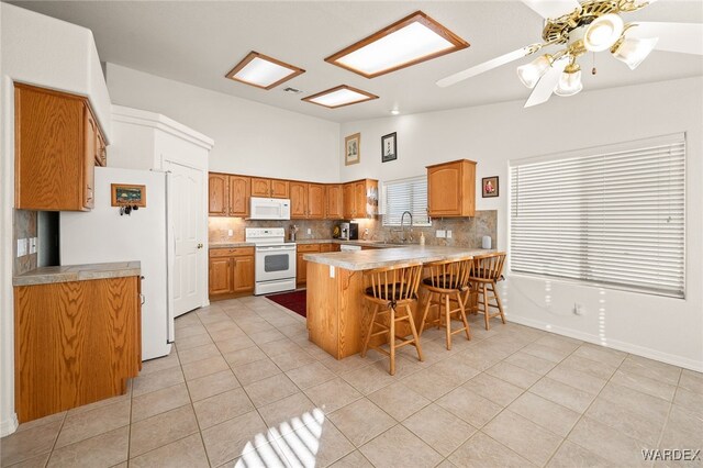 kitchen with a breakfast bar area, light countertops, a sink, white appliances, and a peninsula