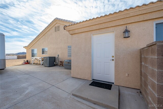 entrance to property featuring a patio area, a tile roof, central AC unit, and stucco siding