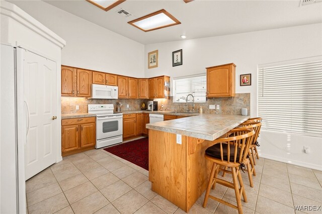 kitchen with visible vents, a sink, white appliances, a peninsula, and a kitchen breakfast bar