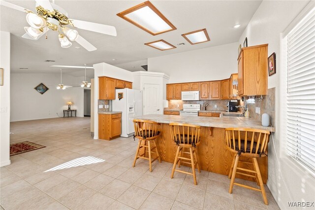 kitchen with brown cabinets, a breakfast bar area, light countertops, white appliances, and a peninsula