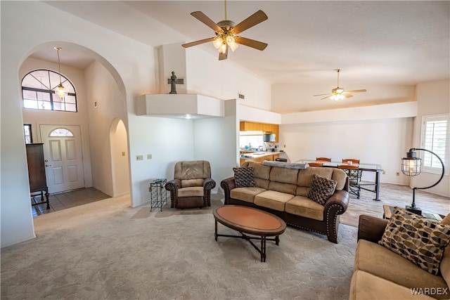 living area featuring light carpet, high vaulted ceiling, arched walkways, and ceiling fan with notable chandelier