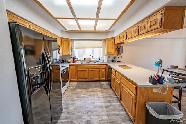 kitchen with light wood finished floors, light countertops, a sink, a peninsula, and black appliances