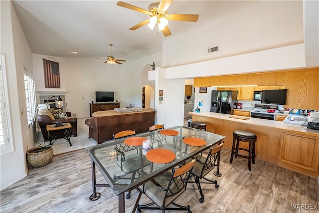 dining room with high vaulted ceiling, visible vents, ceiling fan, and light wood finished floors