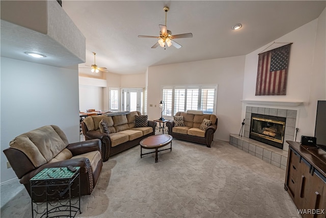 living room with light carpet, a tiled fireplace, lofted ceiling, and a ceiling fan