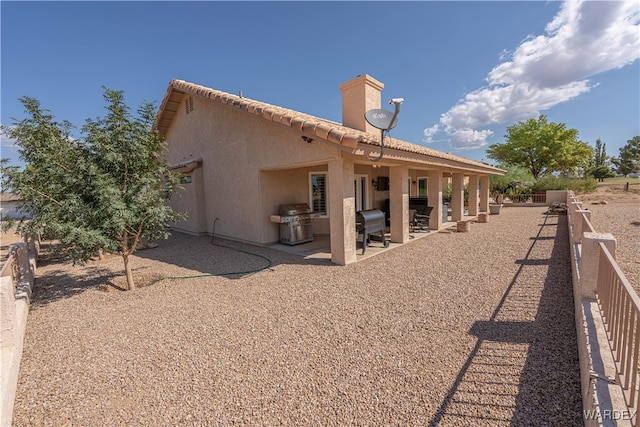 rear view of house featuring a patio, fence, a tiled roof, stucco siding, and a chimney