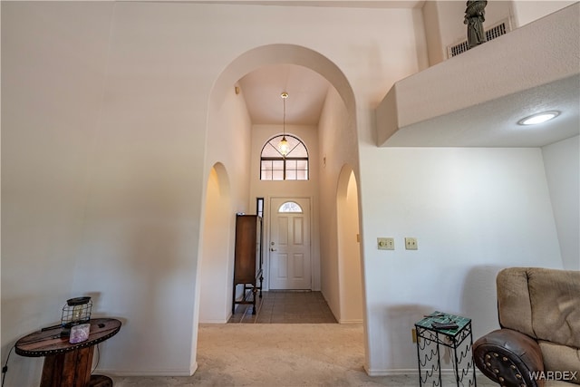 entryway with arched walkways, light colored carpet, a high ceiling, visible vents, and baseboards