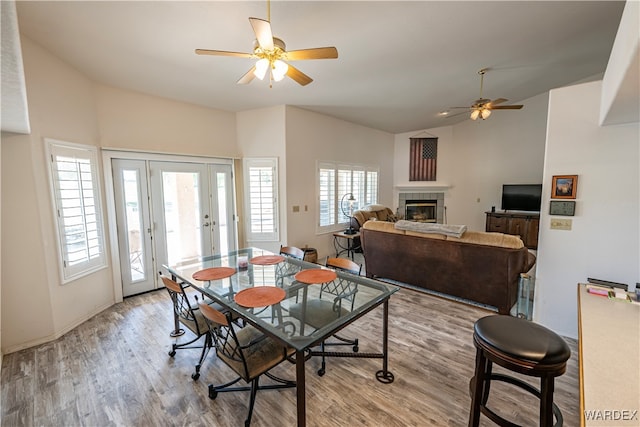 dining room featuring light wood-style floors, lofted ceiling, a fireplace, and a ceiling fan