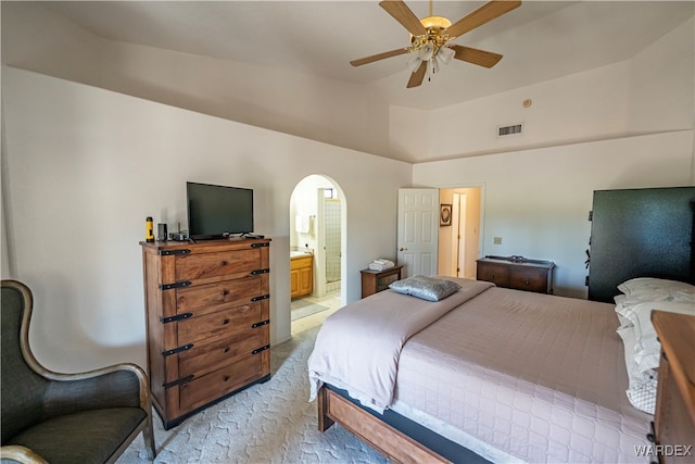 bedroom featuring visible vents, arched walkways, light colored carpet, ensuite bathroom, and vaulted ceiling