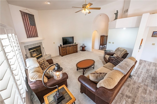 living room with visible vents, arched walkways, a ceiling fan, a tile fireplace, and a high ceiling